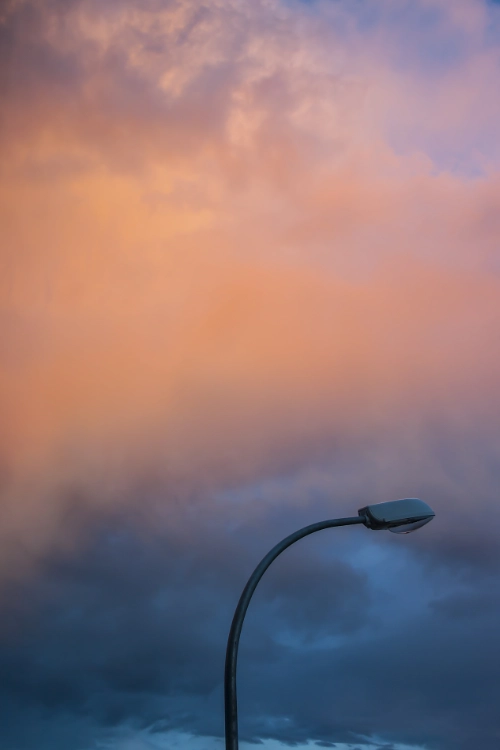 cloudy sky at sunset showing colours of orange at the top and steel blue at the bottom. the lower third of the image features a lamppost.