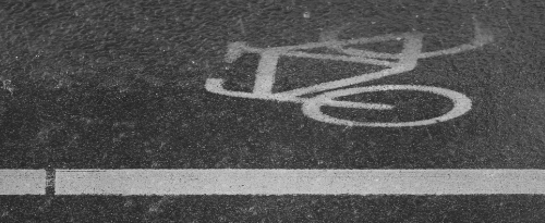 a pictographic marking of a bike lane - showing a bicycle, partly covered by water due to heavy rain on dark grey asphalt.
