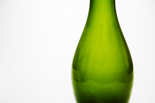 an iridescent grass green vase positioned in the right third of the image with an all white background.